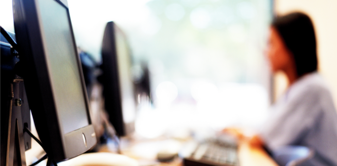 side view of computers on a desk with a young woman in the background