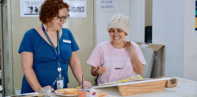 clinician looking on as a smiling young woman paints