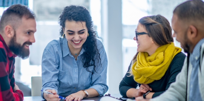 four smiling young people working at a table