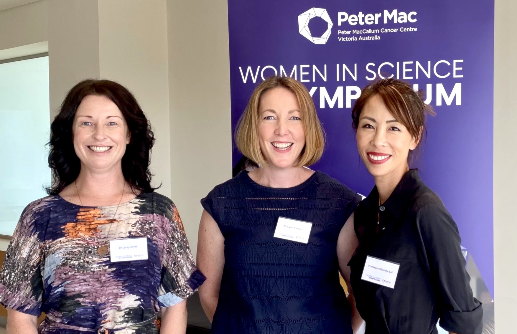 Three female researcher leaders posing and smiling in front of Peter Mac banner
